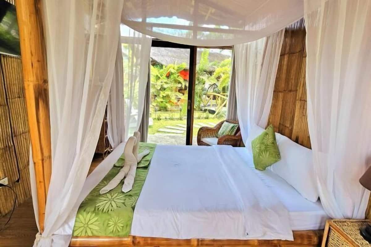 A bed with a canopy, a green patterned bedspread, and a view of a garden through a glass door.