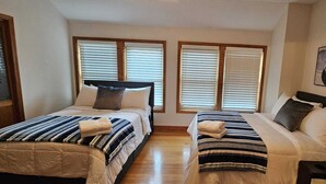 A double room with two beds, each with a striped blanket and pillows, wooden headboards, and large windows with blinds. - Vacation, Wedding, Retreat & Family Gathering, Spa and Theater rooms - Sleeps 30 (Manchester)