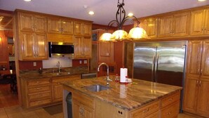 A kitchen with wooden cabinets, a stainless steel refrigerator, a granite countertop, and a built-in sink. - Vacation, Wedding, Retreat & Family Gathering, Spa and Theater rooms - Sleeps 30 (Manchester)