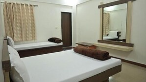 A hotel room with a bed, a small table, a mirror, and a door.