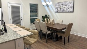 A dining area with a wooden table and chairs, a kitchen with a granite countertop, and a ceiling light fixture.