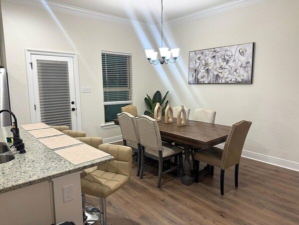 A dining area with a wooden table and chairs, a kitchen with a granite countertop, and a ceiling light fixture.