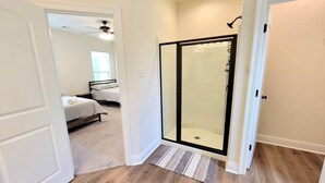 A room with a wooden floor, a glass shower enclosure, and a bed with a white headboard.