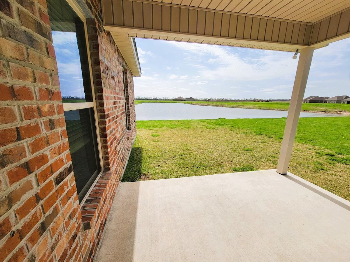 A covered patio with a view of a grassy area and a body of water.