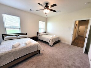 Une chambre avec deux lits, un ventilateur de plafond et une porte donnant sur une autre pièce.