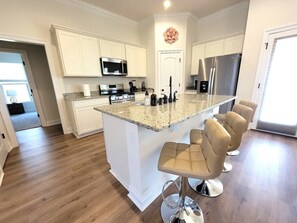 A modern kitchen with a central island, bar stools, stainless steel appliances, and white cabinetry. - Cajun Stay at Golden Horizon Pond Escape -  WCN176 (Calcasieu Parish)