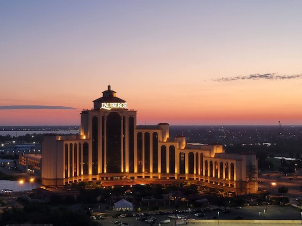 A large hotel with a prominent tower and illuminated signage, surrounded by parking and a body of water.