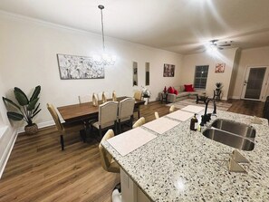 Una cocina moderna con encimeras de granito, un lavamanos de acero inoxidable y un comedor con mesa y sillas de madera.