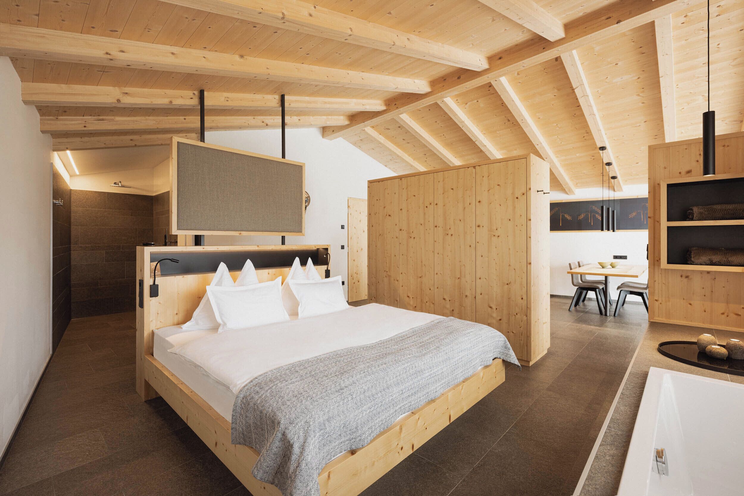 A wooden bedroom with a bed, a desk, and a bathroom.