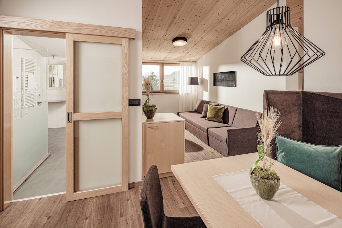 Een modern interieur met een houten plafond, een eethoek met tafel en stoelen, een bank met kussens en een hanglamp.