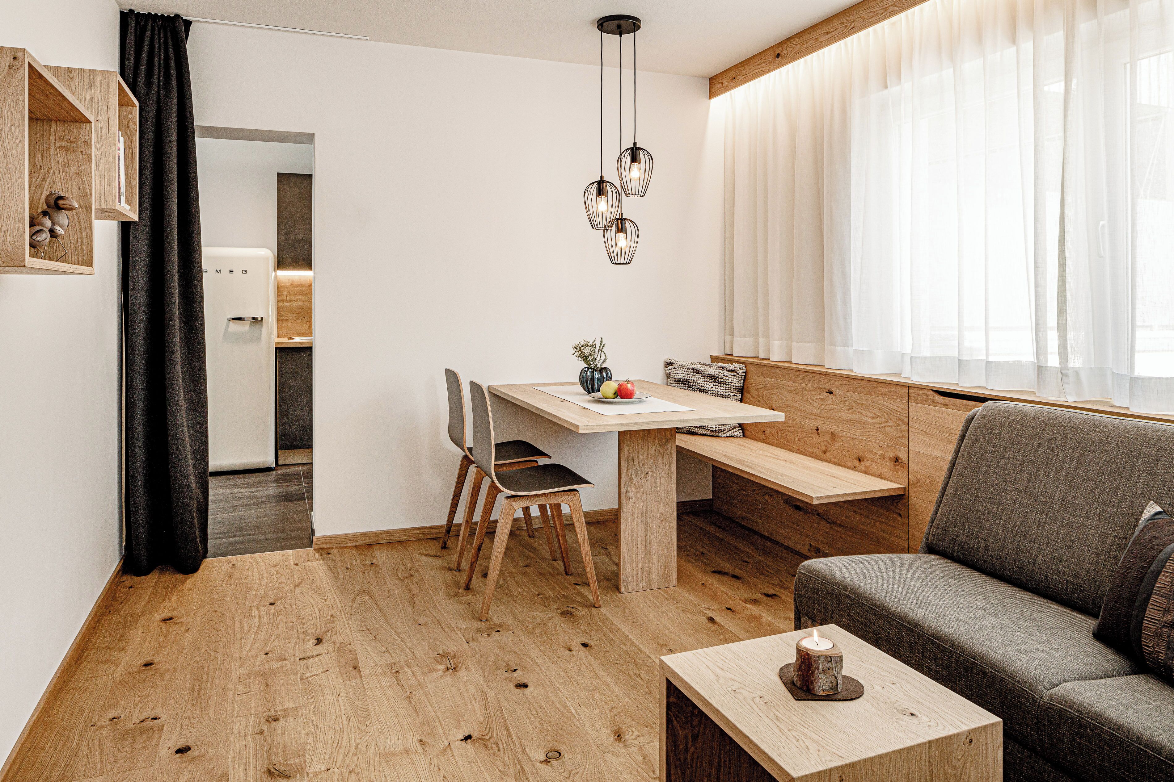Un salon moderne avec un plancher en bois, un canapé, une table à manger avec des chaises, un luminaire suspendu et, au fond, un coin cuisine.