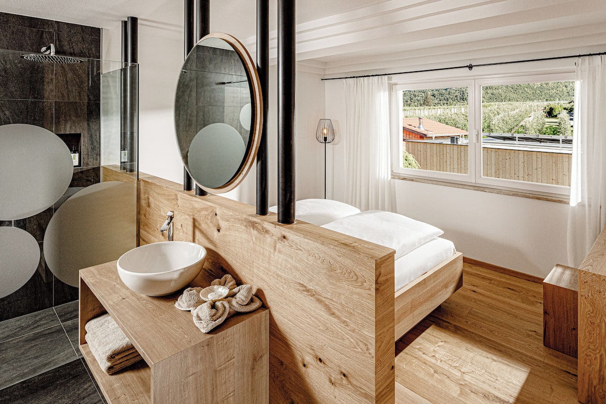 Een moderne badkamer met een houten wastafel, een grote spiegel, een rond wastafelmeubel en een douchegedeelte.