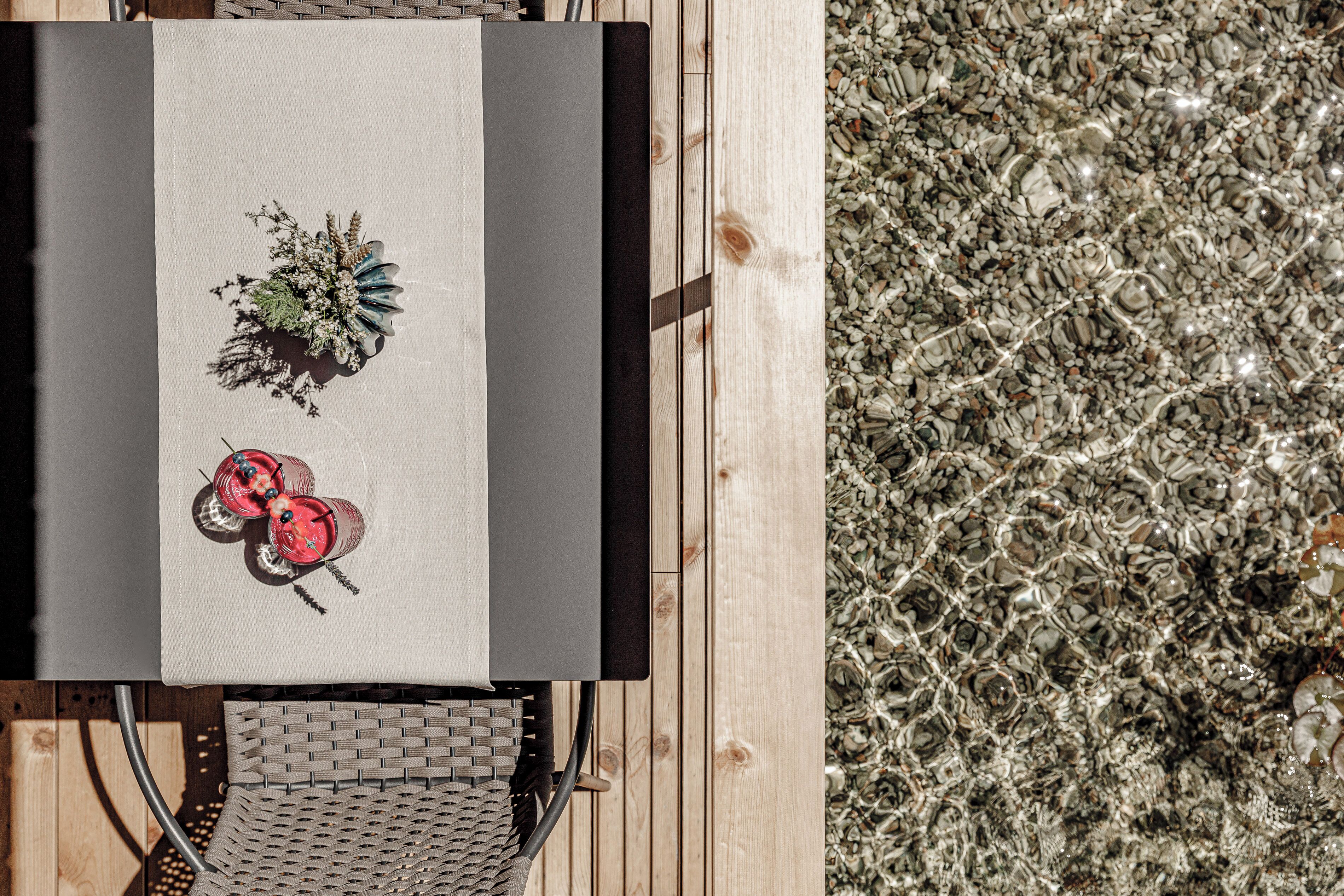 A table with a floral centerpiece and a red decorative item, set on a wooden deck with a pebbled surface.