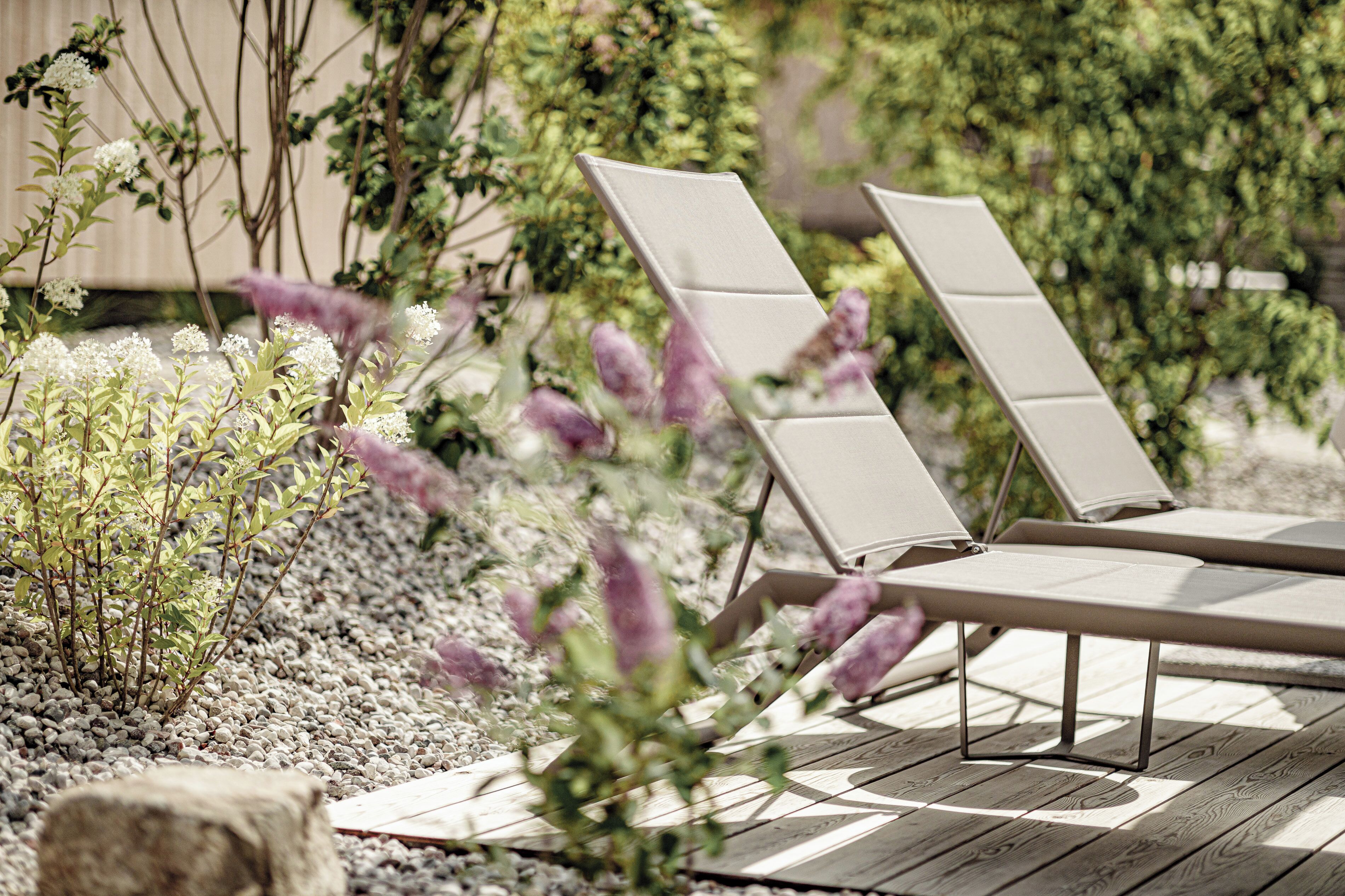 Une terrasse dotée de deux chaises longues et d’une petite table, entourée de gravier et de plantes.