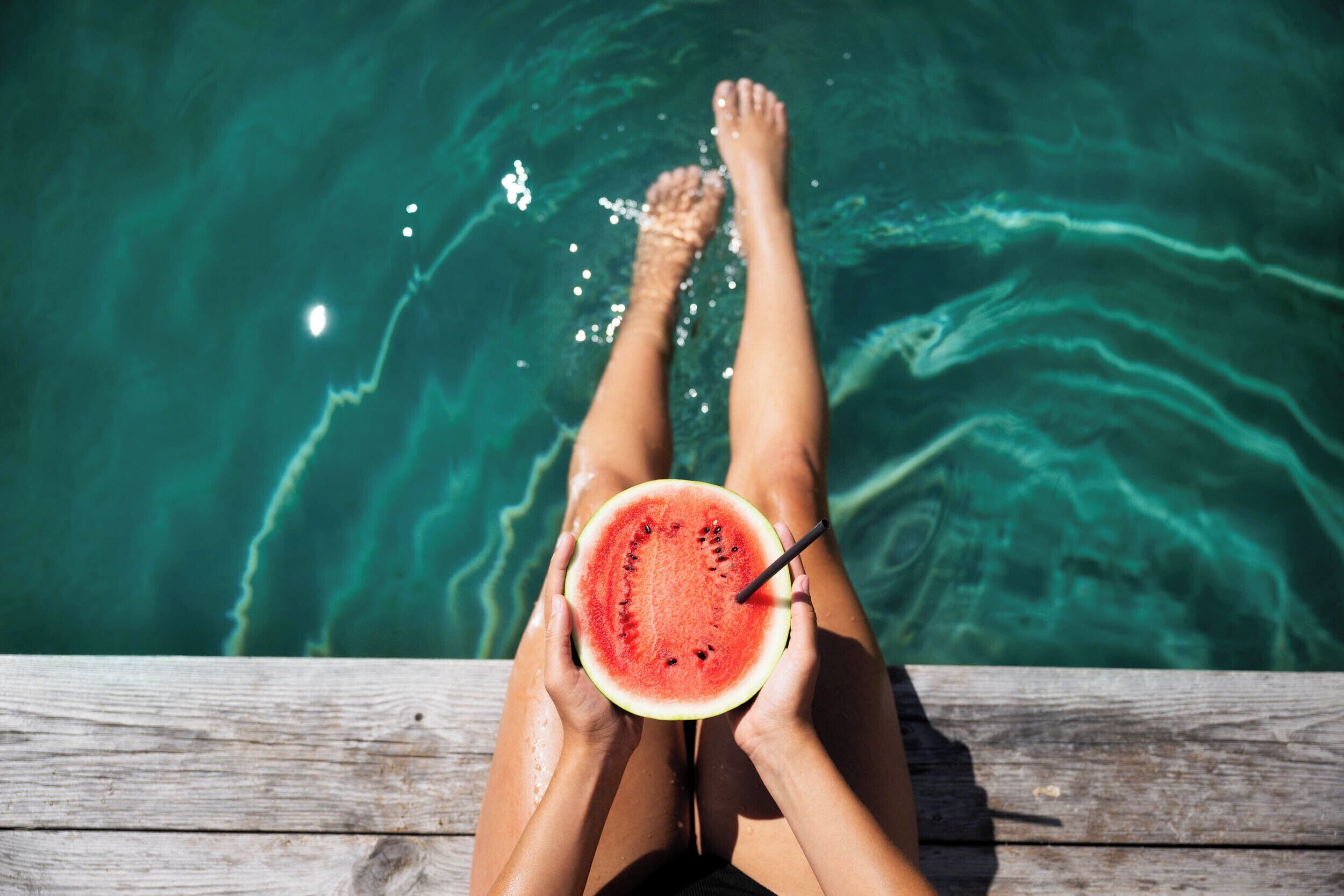 A person sitting by a pool with a watermelon slice in hand.