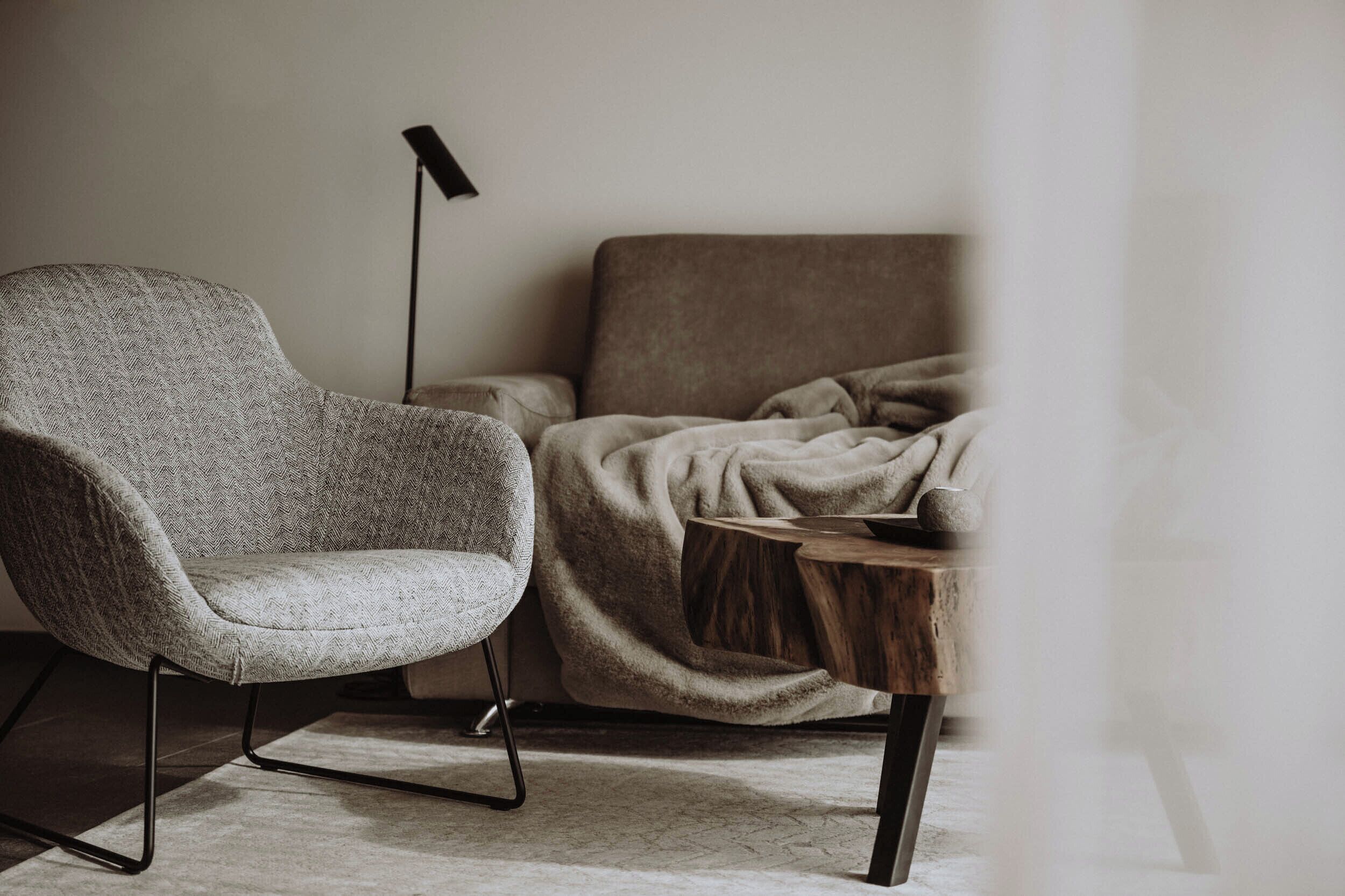 A modern room with a herringbone-patterned armchair, a wooden side table, and a large, dark floor lamp.