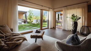 Un vaste salon doté d’une grande porte-fenêtre coulissante donnant sur une terrasse extérieure. On y trouve un coin salon confortable avec un canapé et des fauteuils, une petite table basse en bois et une plante en pot.