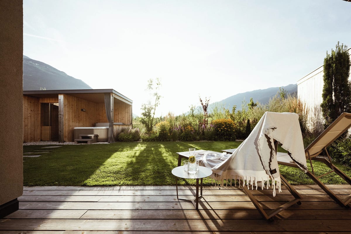 Een houten terras met een tafel en stoelen, een overdekt gedeelte en uitzicht op een berg en tuin.