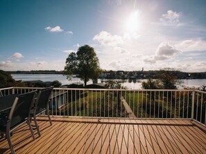 A deck with chairs overlooking a lake, a tree, and a distant town.