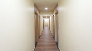 A long, narrow hallway with wooden flooring and beige walls. - JPS Palm Inn, Near Maruti Suzuki Manesar (Gurugram)