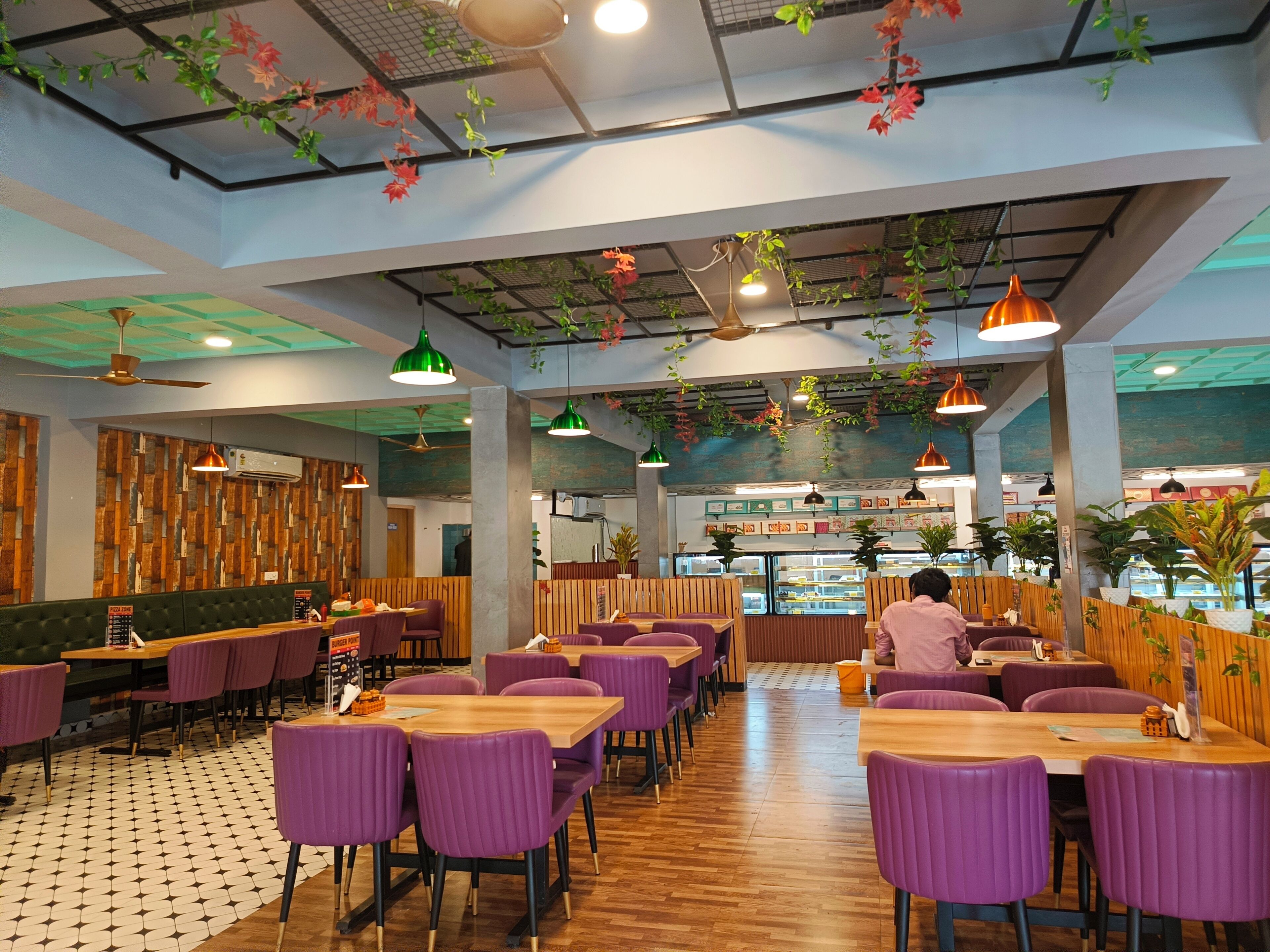 A restaurant with wooden flooring, purple chairs, and green hanging plants.