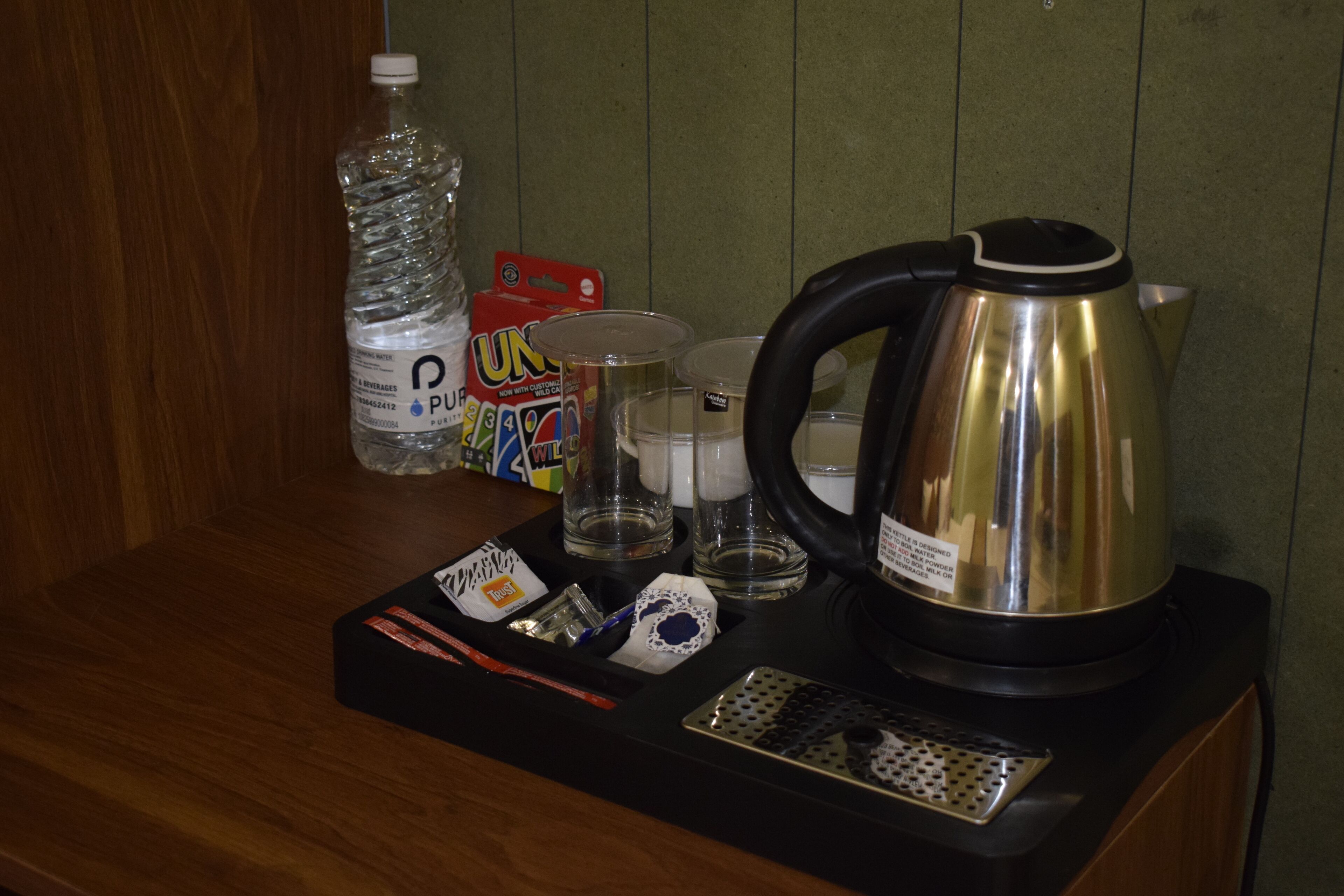 A kitchen counter with a kettle, a bottle of water, a box of tea bags, and a tray with utensils.