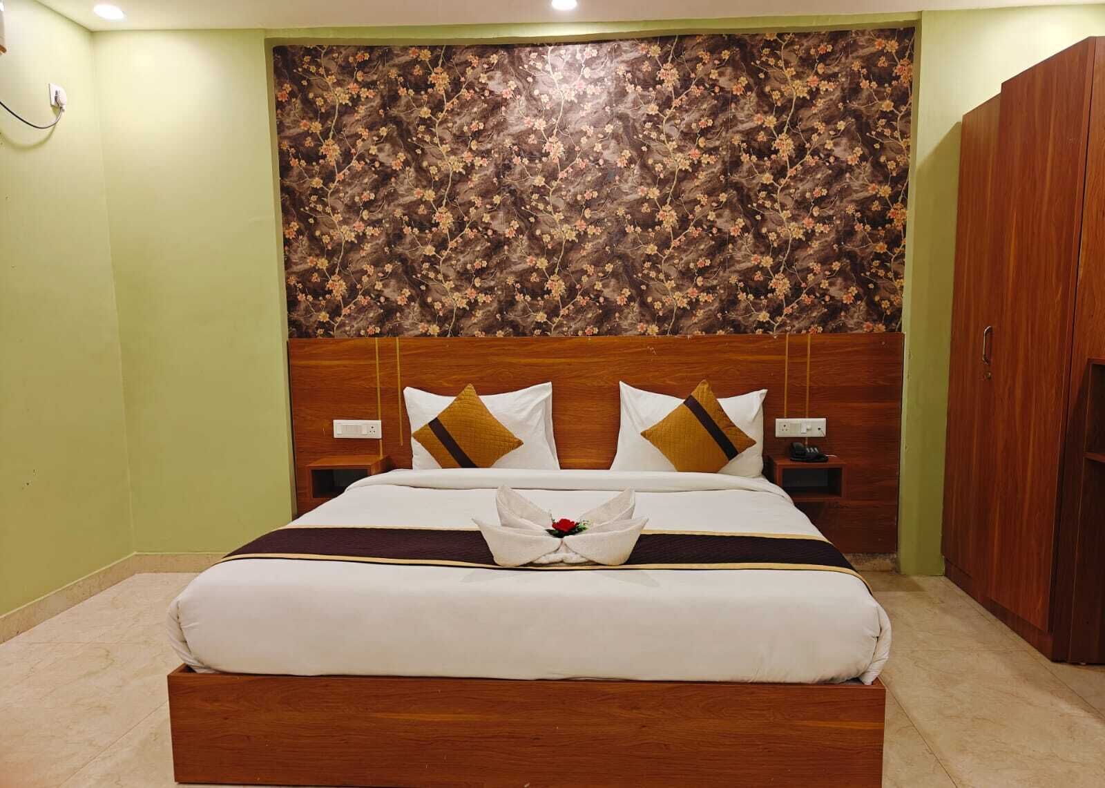 A neatly made bed with a floral headboard, a wooden wardrobe, and a bedside table with a lamp.