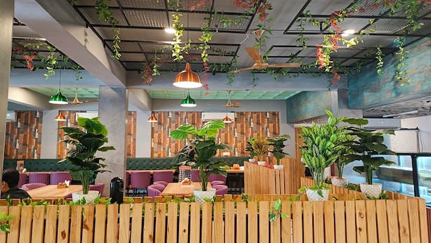 A modern restaurant interior with wooden furniture, hanging plants, and pendant lighting. - JPS Palm Inn, Near Maruti Suzuki Manesar (Gurugram)