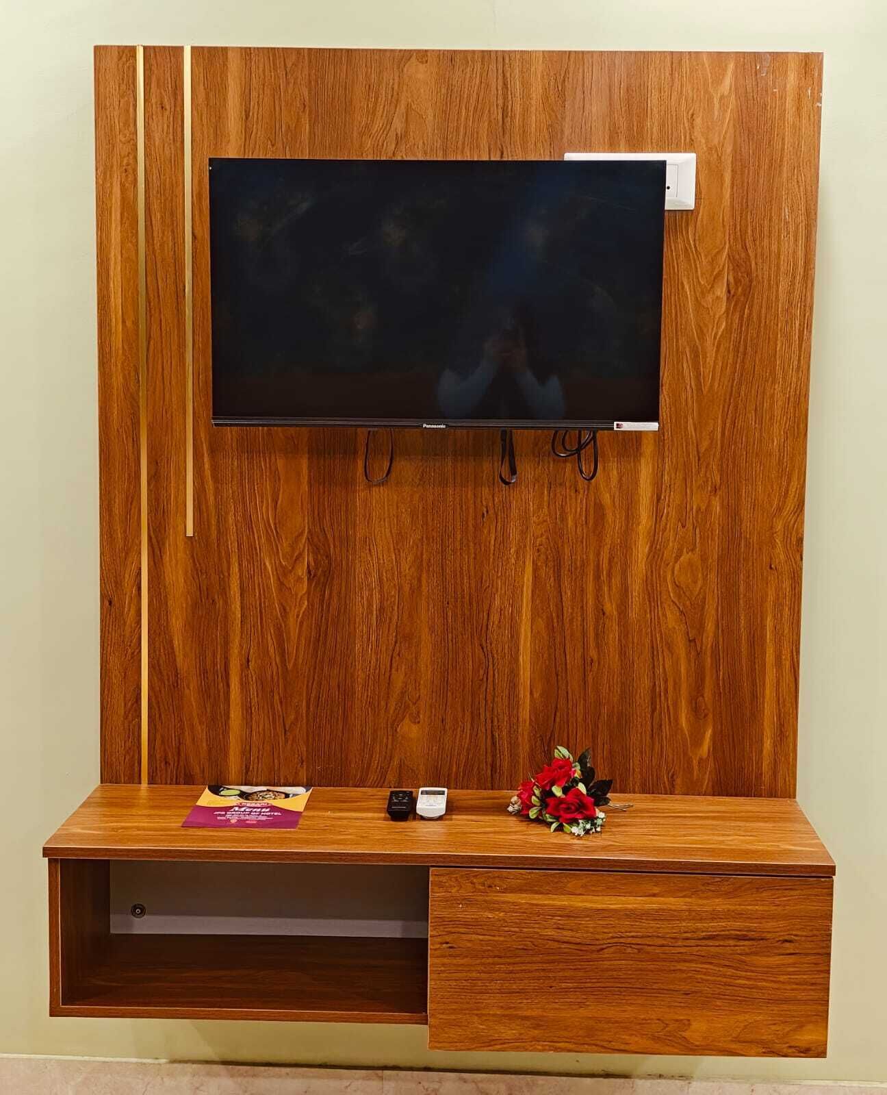 Un mueble de televisión de madera con un televisor de pantalla plana montado encima, un cajón pequeño y algunos objetos sobre la superficie.