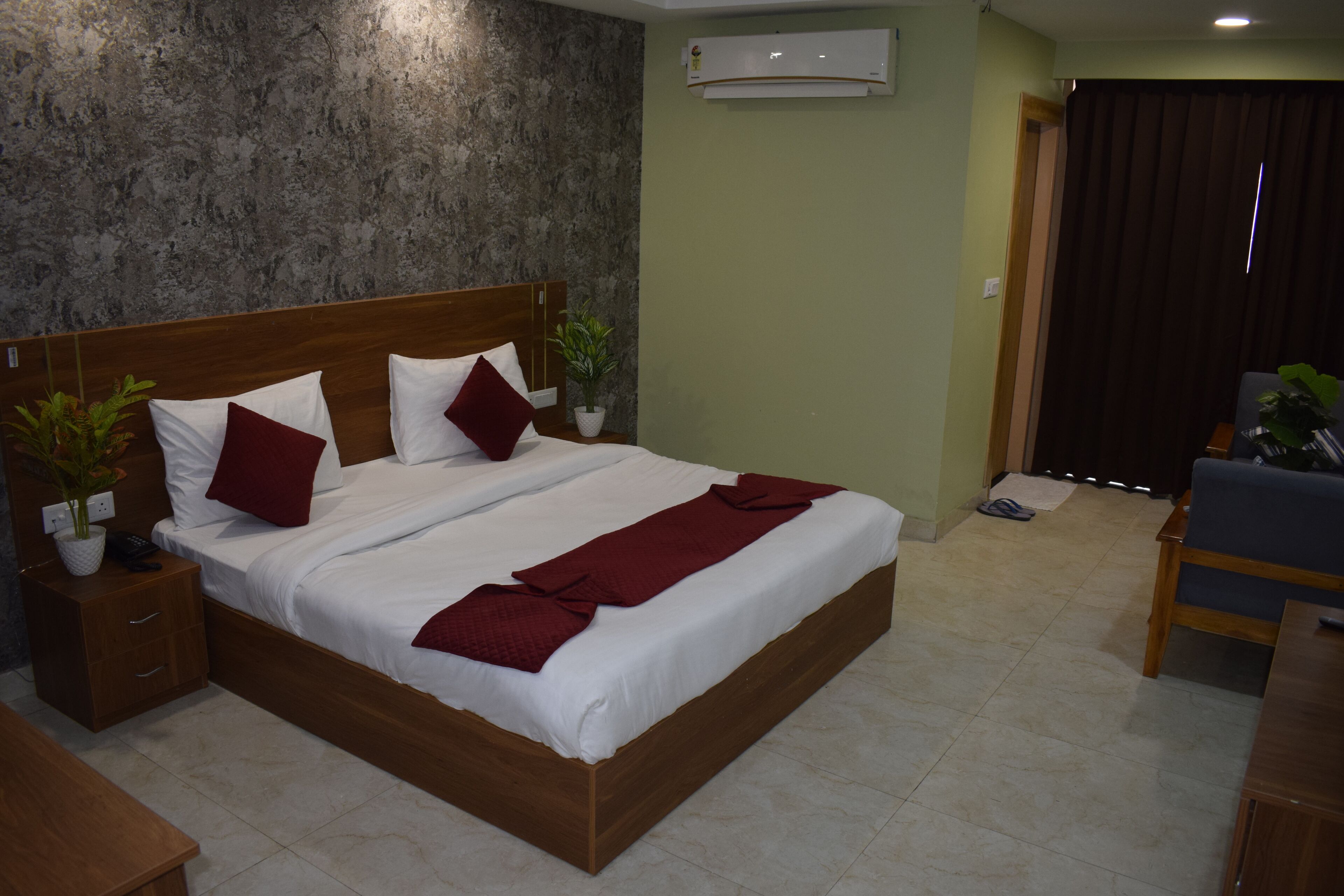 A neatly made bed with white and red bedding, a wooden headboard, and two potted plants.