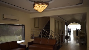 A spacious lobby with a staircase, a large window, a brown leather sofa, and a chandelier. - JPS Palm Inn, Near Maruti Suzuki Manesar (Gurugram)