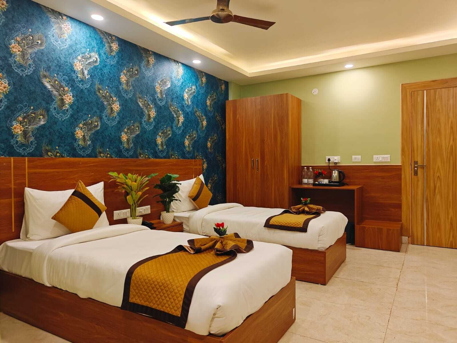 A hotel room with two beds, a wooden wardrobe, a small table with a kettle, and a decorative wall.