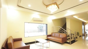 A modern lobby with a sofa, a coffee table, a large window, and a staircase. - JPS Palm Inn, Near Maruti Suzuki Manesar (Gurugram)