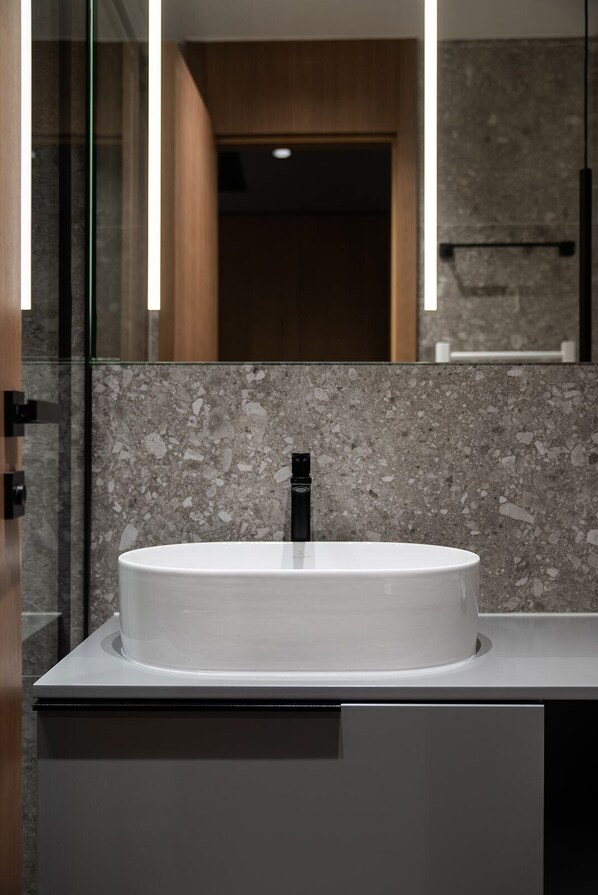 Un baño moderno con un lavamanos blanco redondo, un grifo negro y un respaldas de mármol.