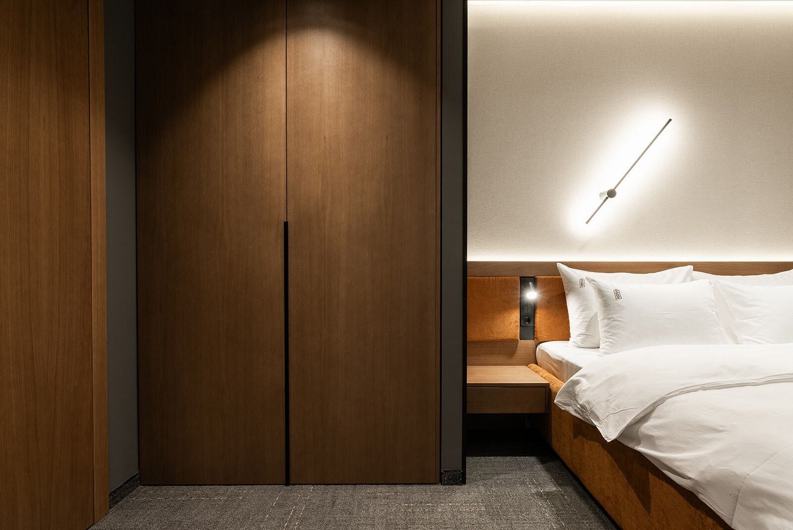 Ein modernes Schlafzimmer mit einem Holzschrank, einem Bett mit weißen Bettwäsche und einem Nachttisch.