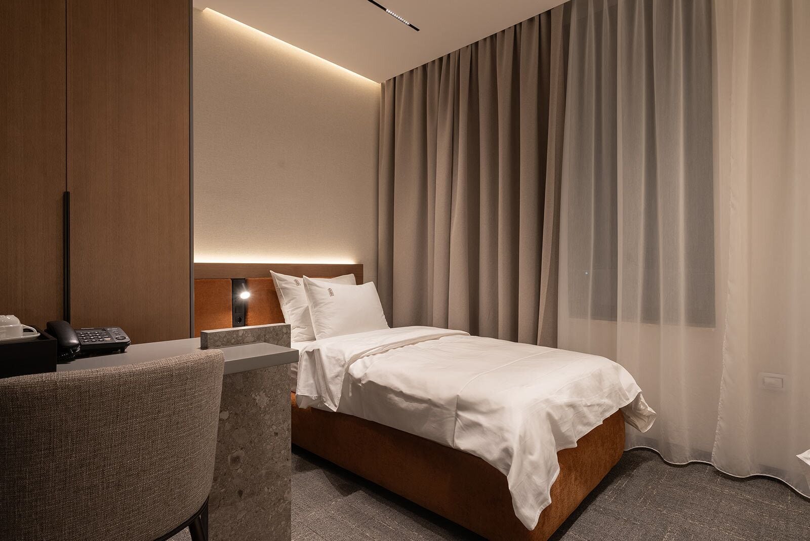 Une chambre d’hôtel avec un lit, un bureau, un téléphone et un rideau.