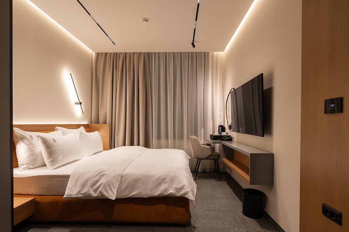 Une chambre d’hôtel moderne dotée d’un grand lit, d’un bureau avec une chaise, d’un téléviseur à écran plat et d’un luminaire au plafond.