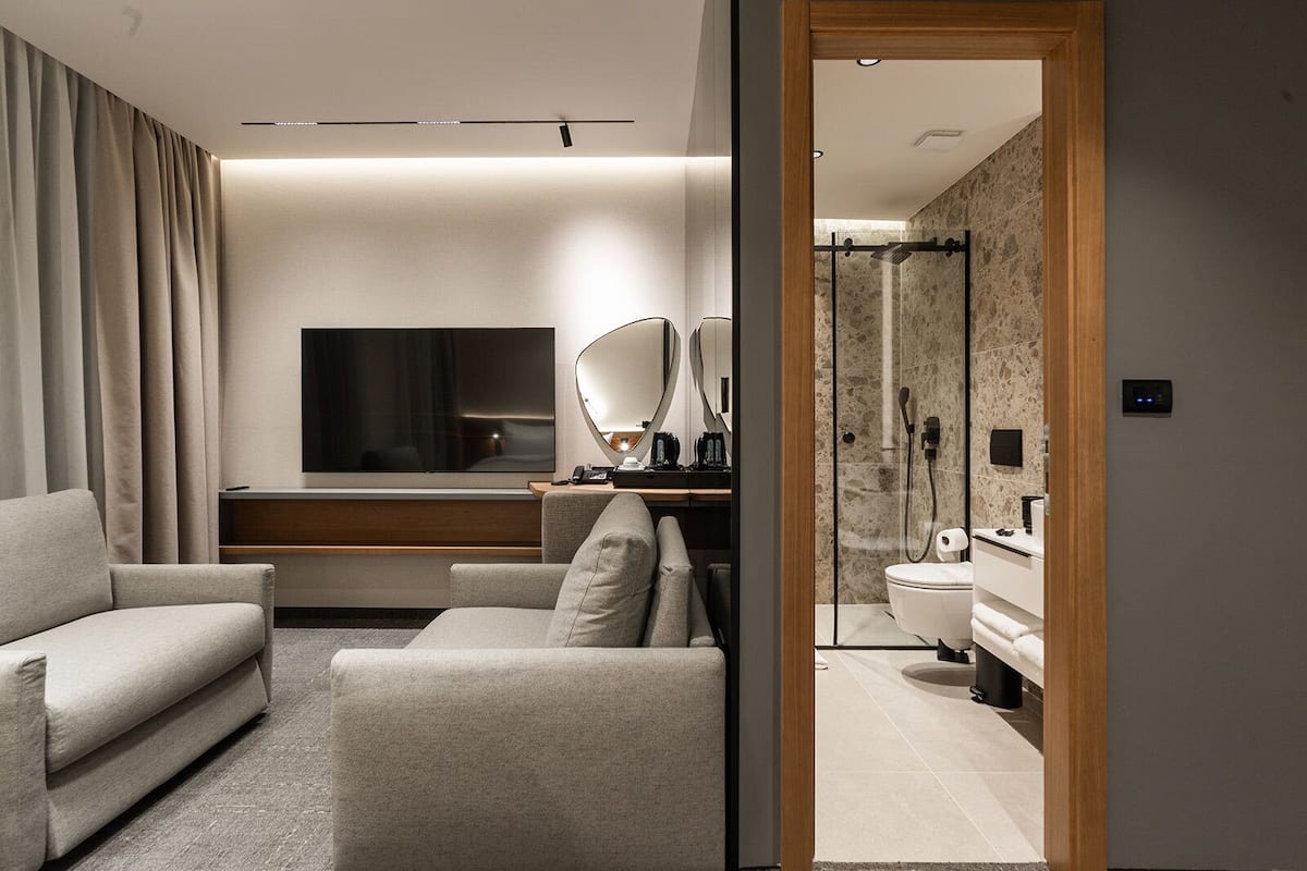 Une chambre d’hôtel moderne équipée d’un canapé, d’une télévision, d’un miroir et d’une salle de bain avec douche et toilettes.