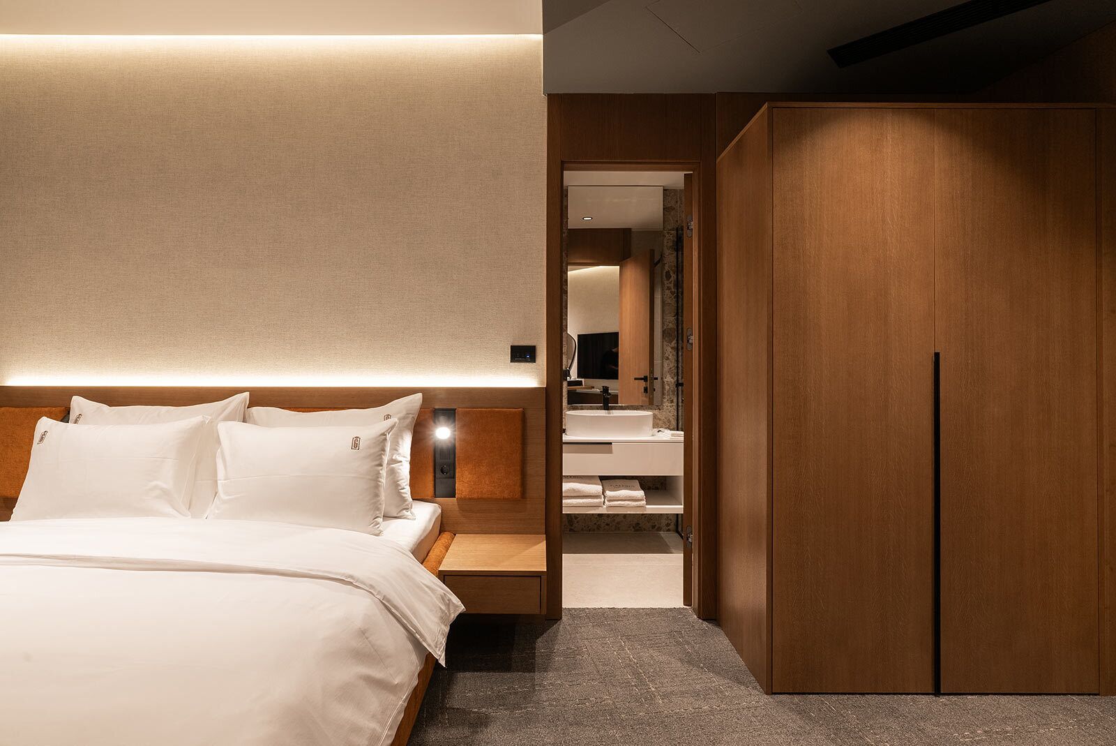 Una camera d'hotel moderna con un letto grande, un armadio in legno e un bagno con lavandino e specchio.