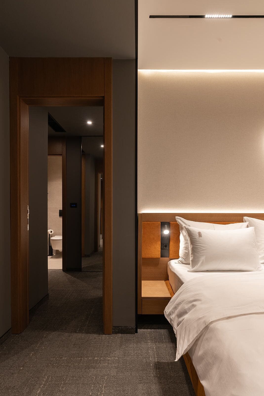 Ein modernes Hotelzimmer mit einem Holzkopfende, einem Nachttisch und einem großen Bett mit weißer Bettwäsche.