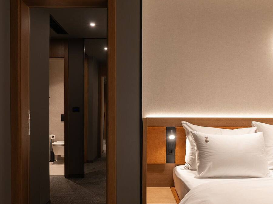 Ein modernes Hotelzimmer mit einem Holzkopfende, einem Nachttisch und einem großen Bett mit weißer Bettwäsche.