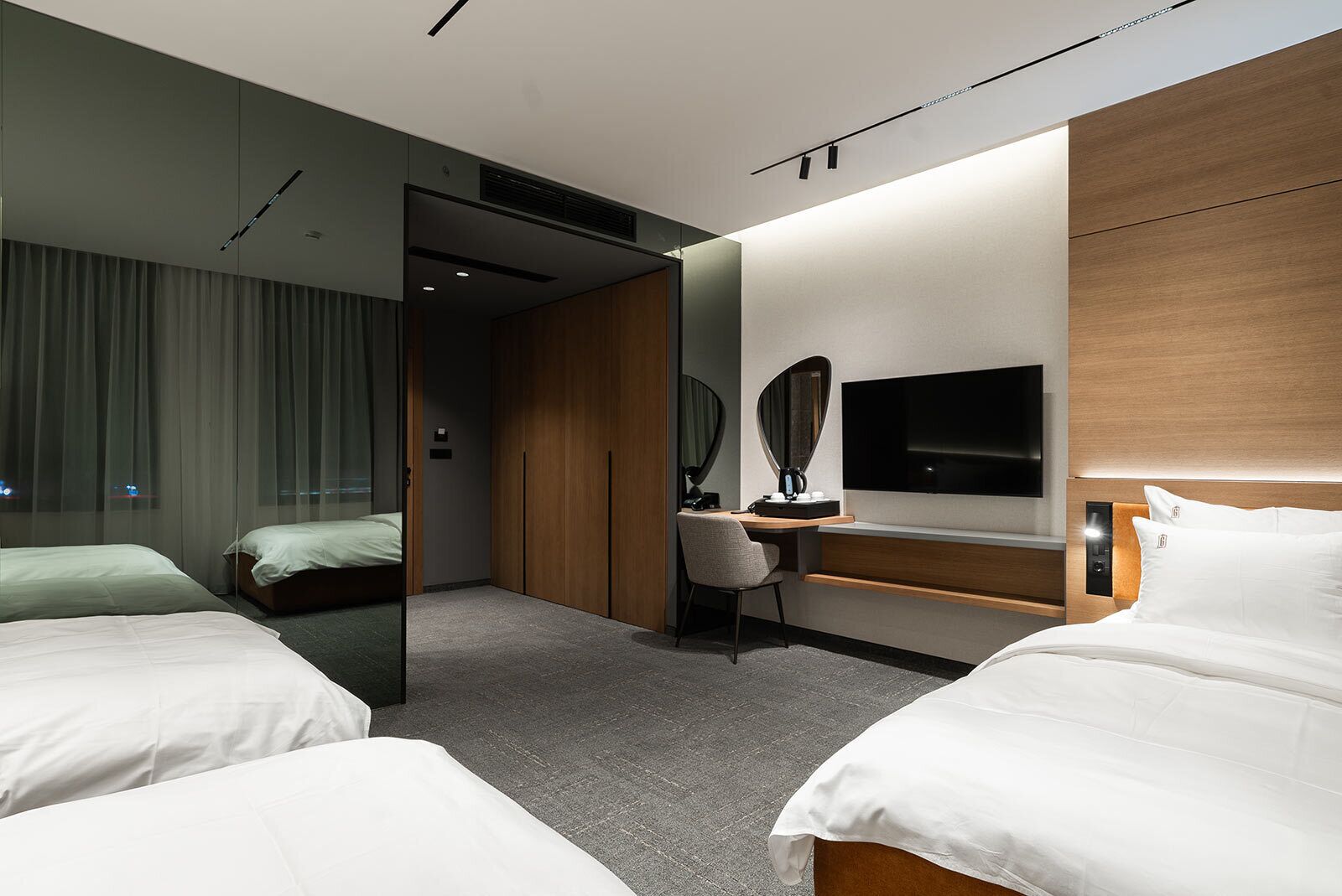 Una habitación de hotel moderna con dos camas, un escritorio, un televisor y un espejo.