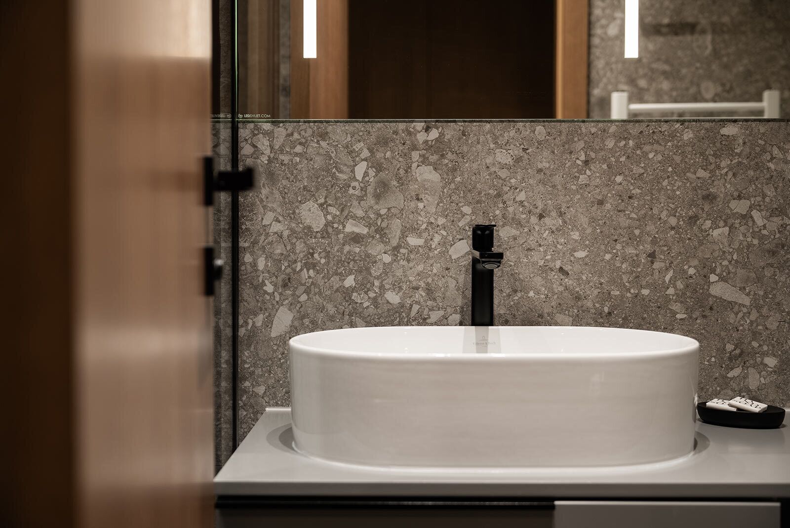 A bathroom with a white sink, a black faucet, and a marble backsplash.