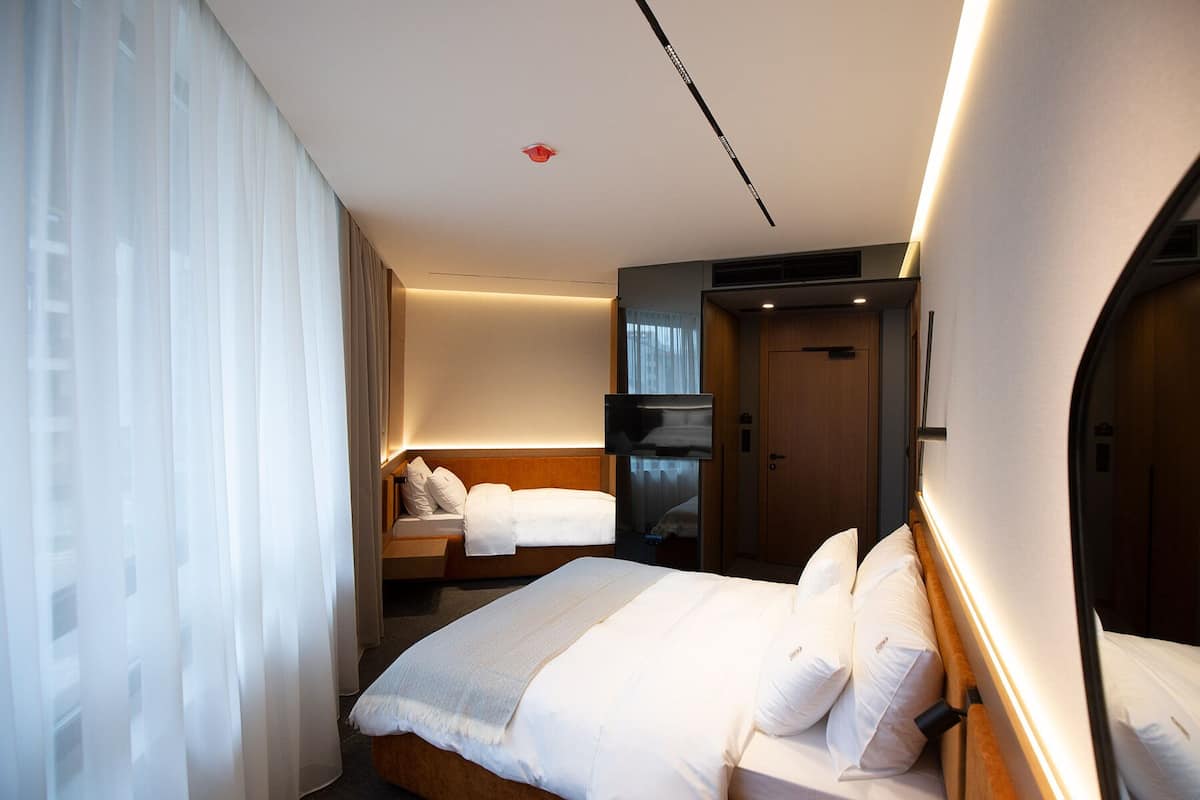 Une chambre d’hôtel moderne avec un grand lit, un plus petit lit, une télévision et une porte de salle de bain.