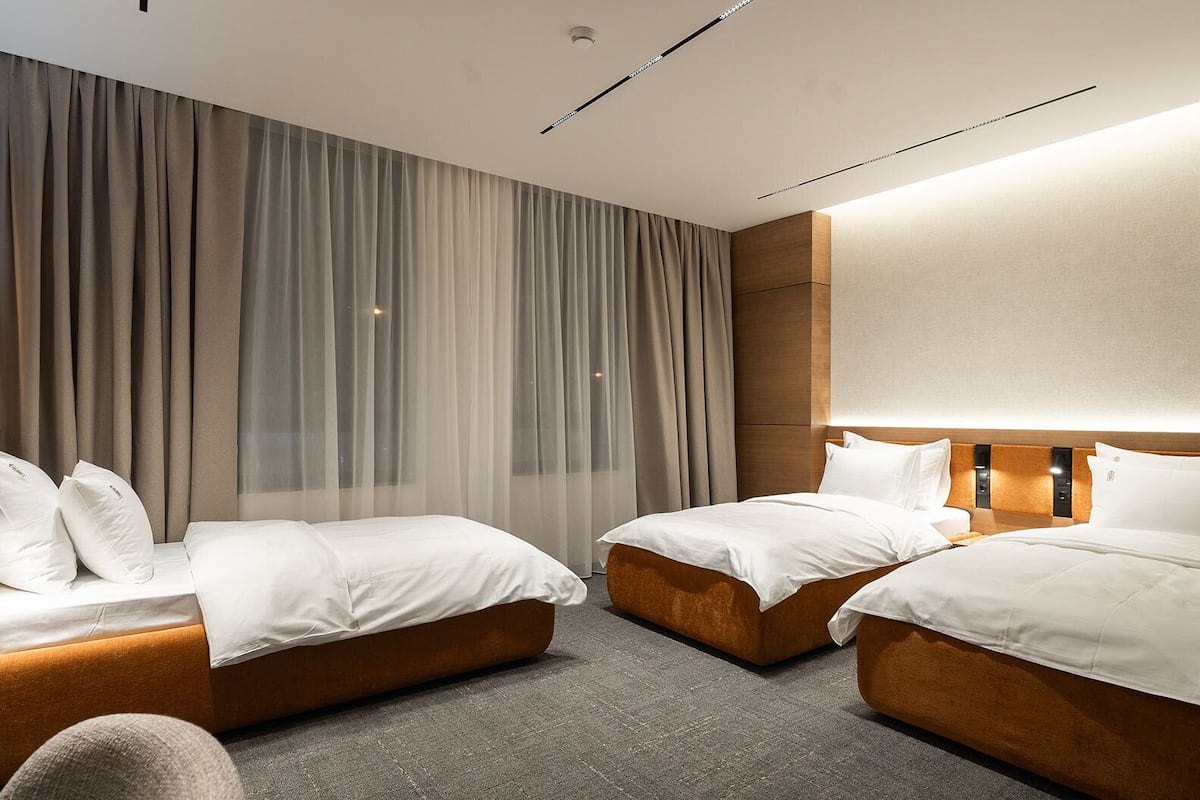 Une chambre d’hôtel moderne avec deux lits, une grande fenêtre avec des rideaux légers et un grand miroir au mur.
