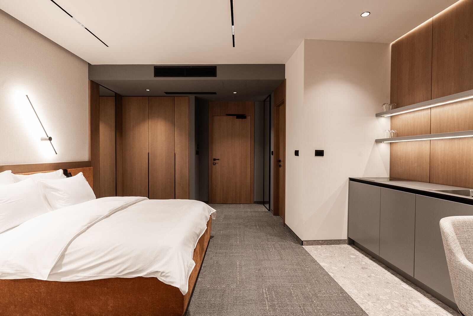 A modern hotel room with a large bed, a kitchenette, and a walk-in closet.
