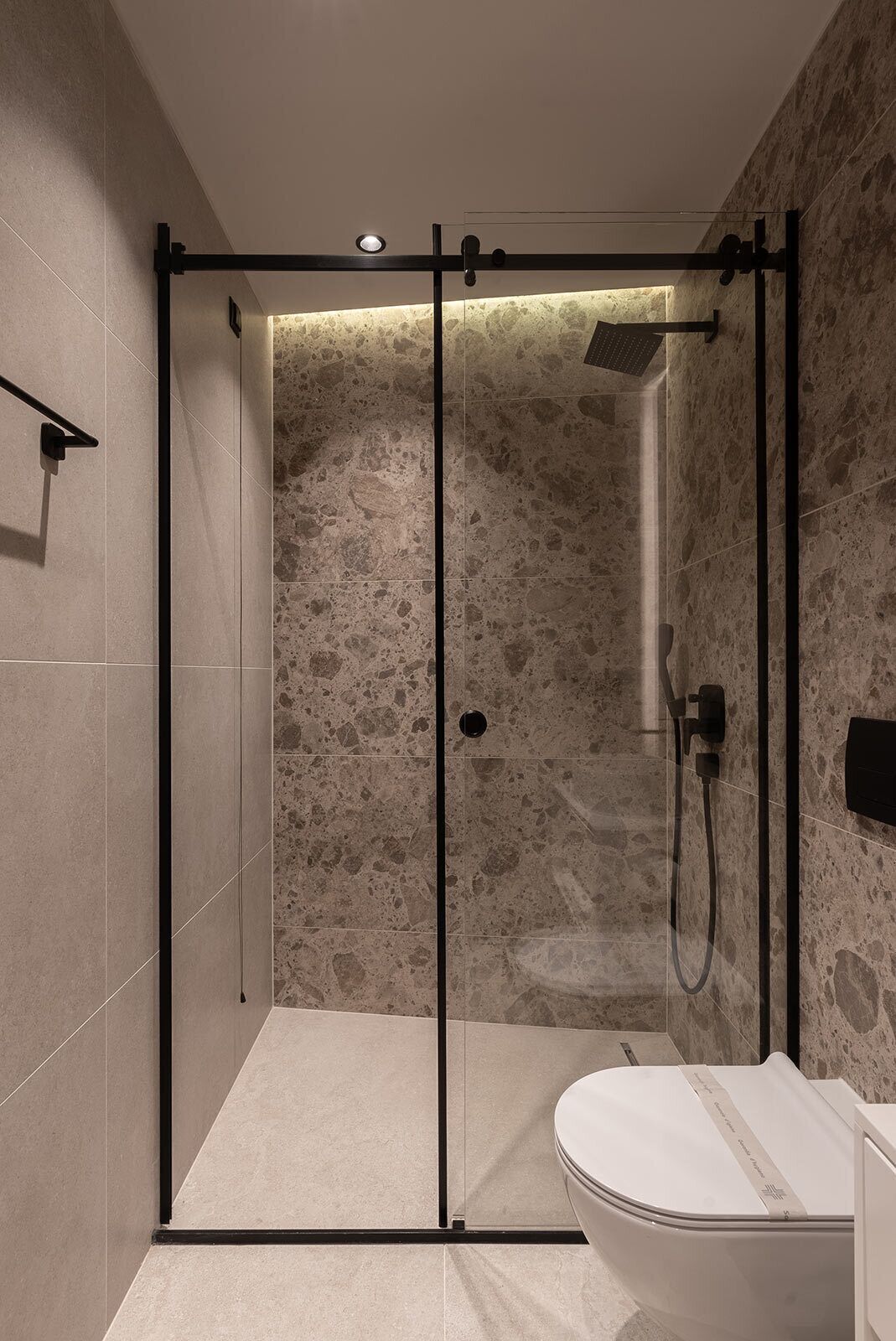 Un baño moderno con ducha envuelta en vidrio, inodoro blanco y pared con textura de piedra.