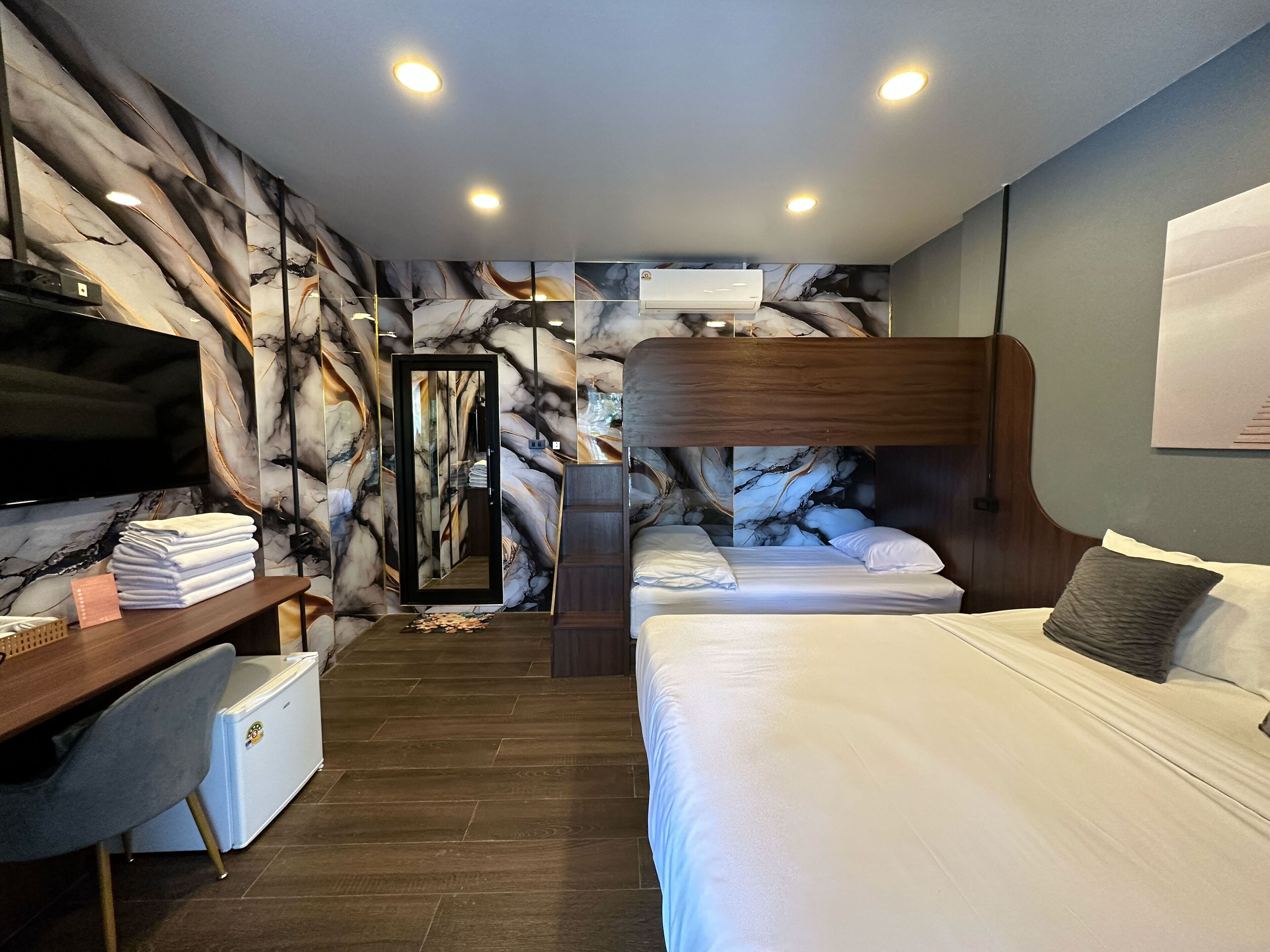 A hotel room with a bed, a desk with a TV, a mirror, and a marble-patterned wall.