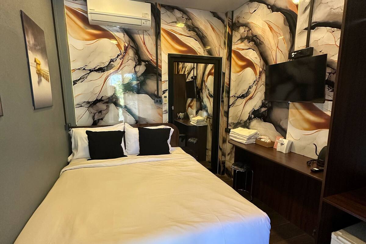 Habitación de hotel con una cama grande, un escritorio y un televisor de pantalla plana, y paredes con diseño de mármol.