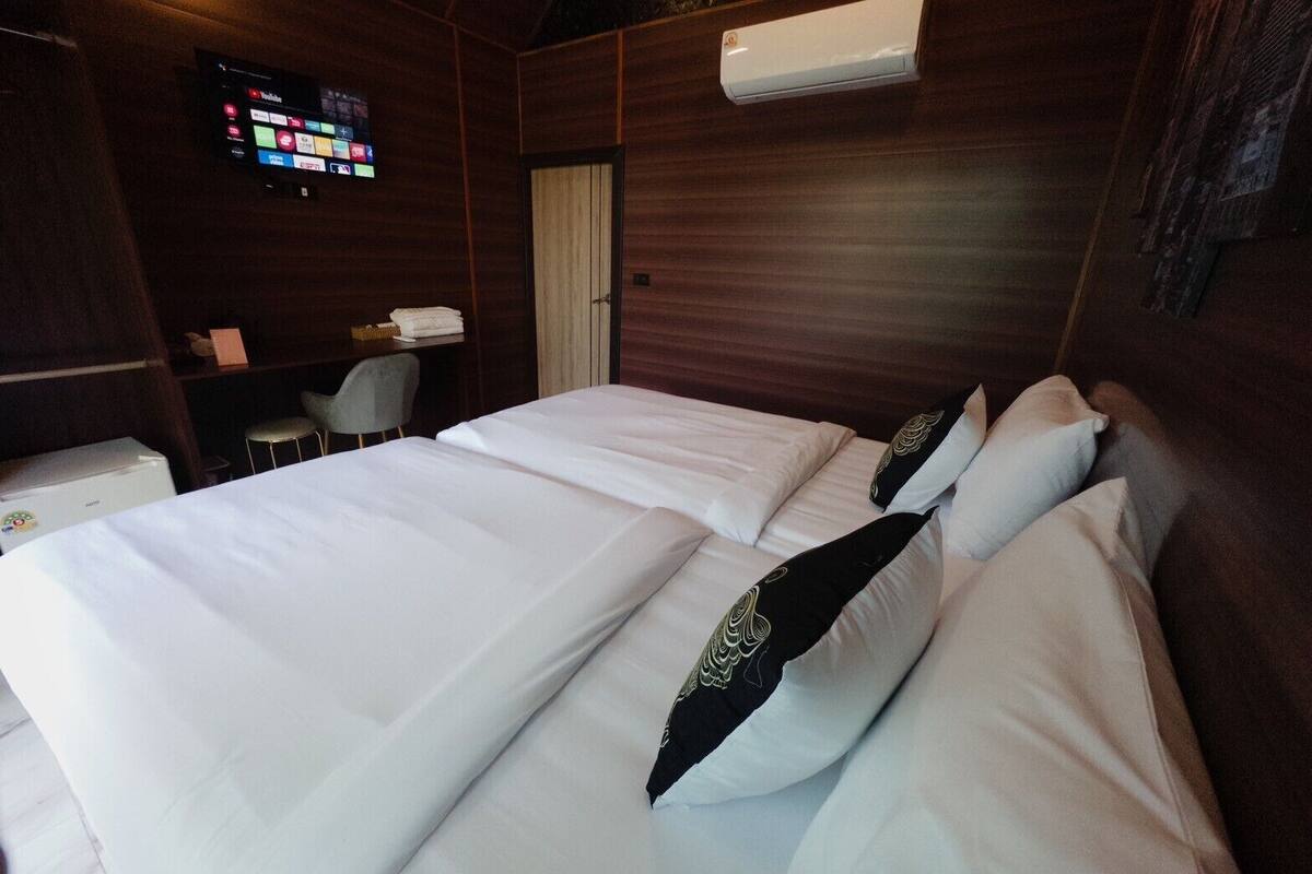 Habitación de hotel con dos camas, un televisor montado en la pared y un escritorio pequeño con una silla.